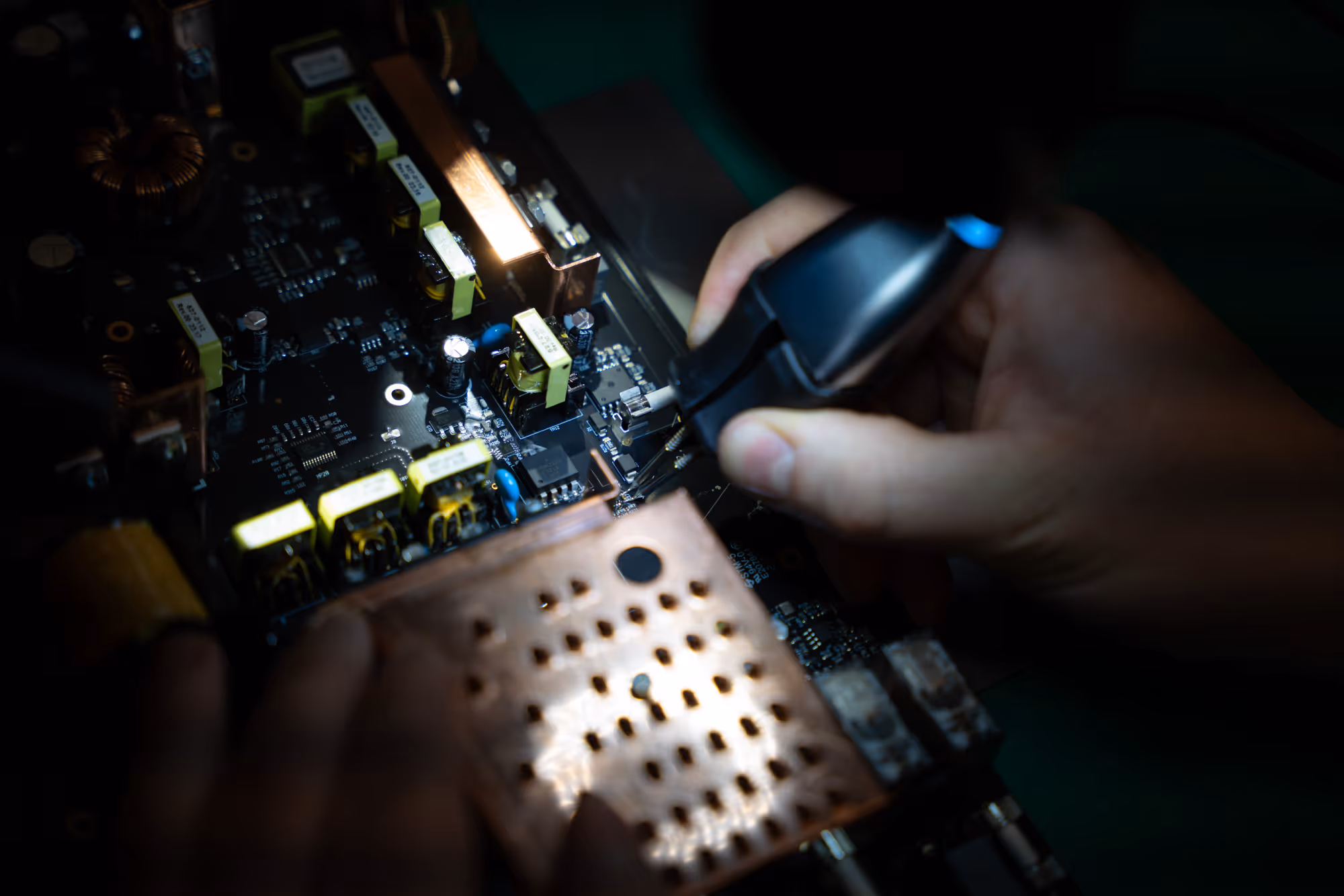 Hand using a soldering iron to work on a detailed electronic circuit board with components.