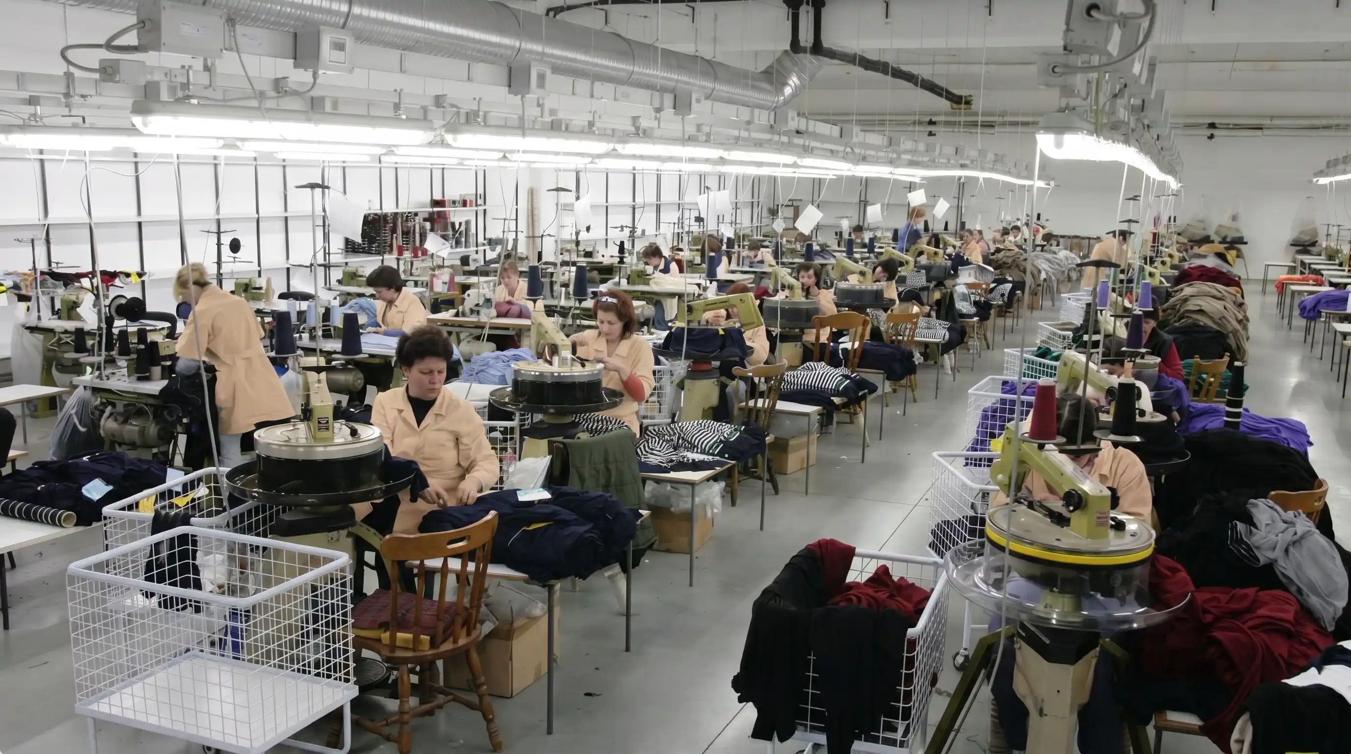 Several workers sewing clothes at machines in a large, bright factory workshop.