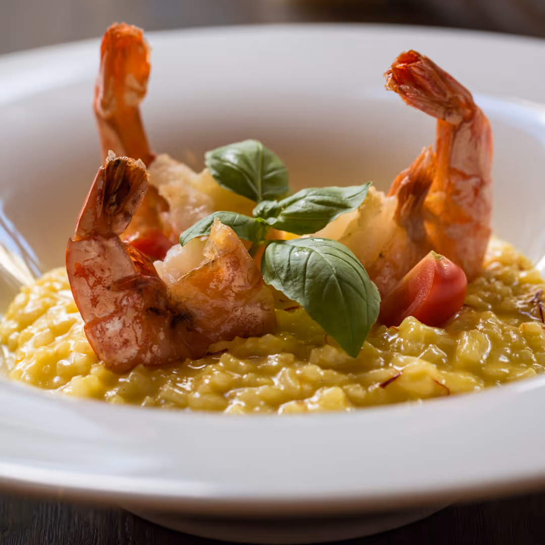 Schale mit Safran-Risotto, garniert mit gebratenen Garnelen, Basilikumblättern und Kirschtomate.