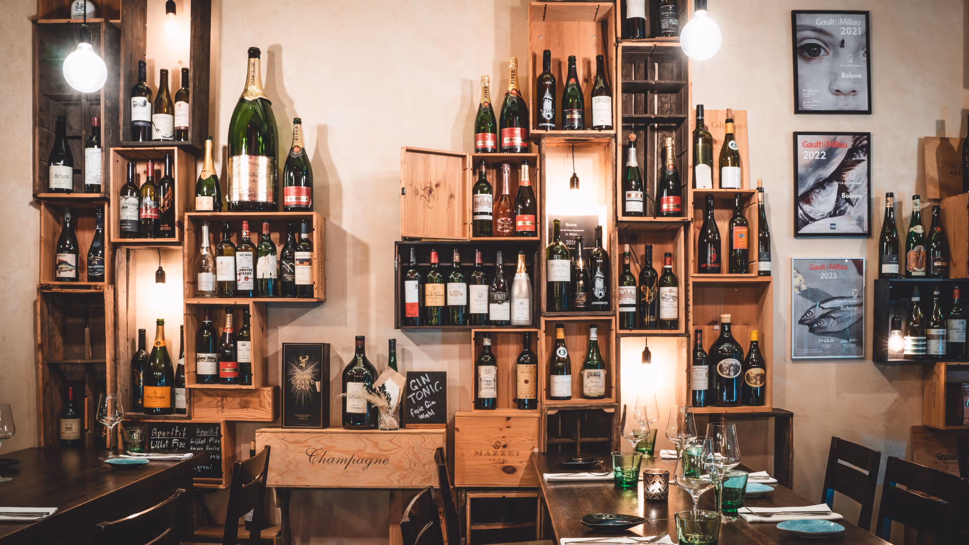 Gemütliches Restaurant mit Holztischen, Weinflaschen in hölzernen Regalen an der Wand und dekorativer Beleuchtung.