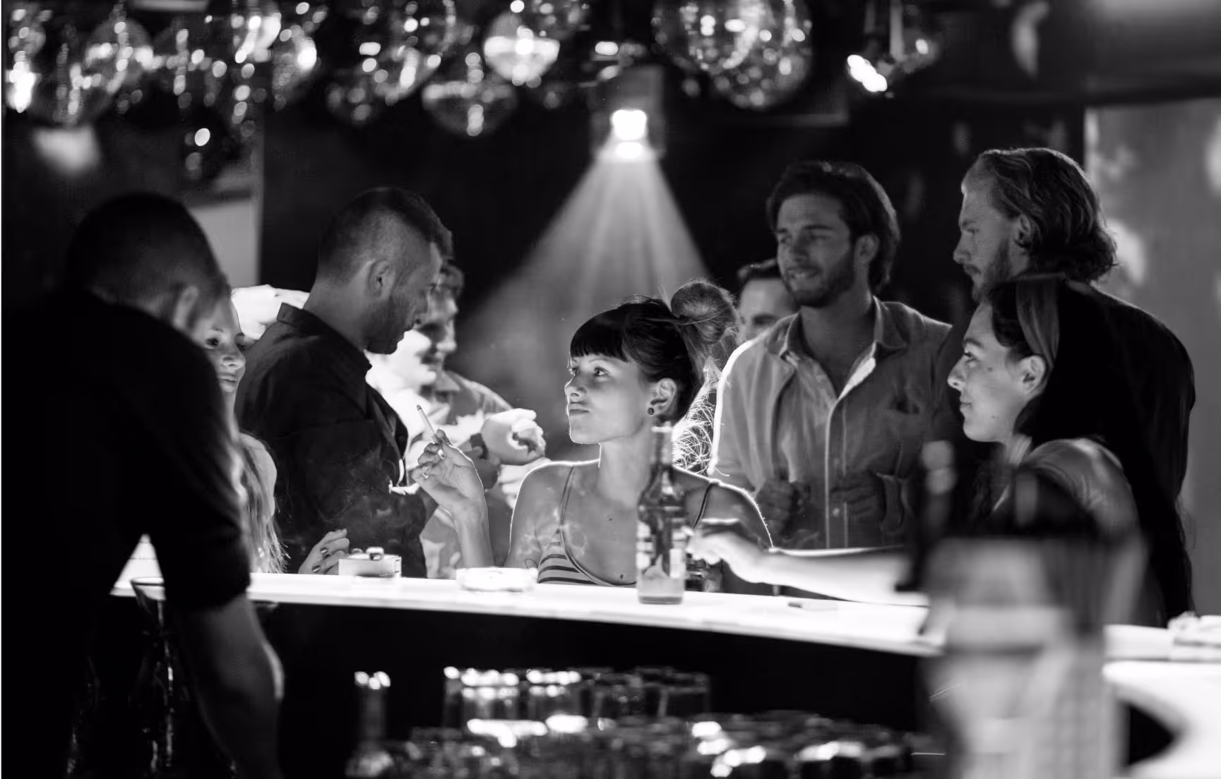 Menschen an einer Bar in einem Club, manche rauchen, andere unterhalten sich und genießen die Atmosphäre.