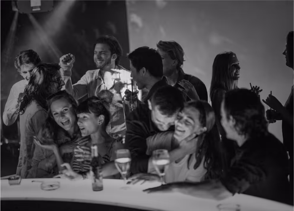 Menschen, die an einer Bar stehend lachen, miteinander reden und Getränke in der Hand halten.