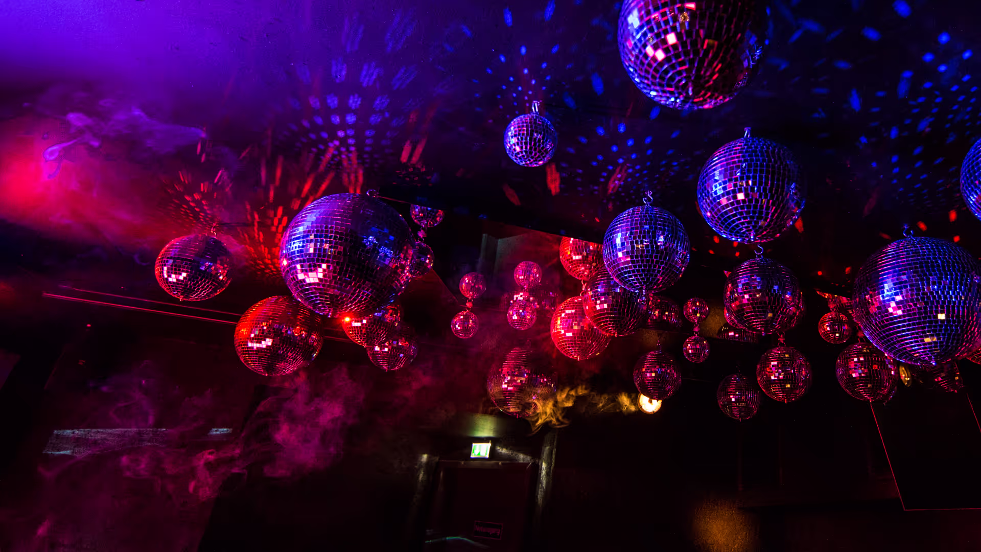 Bunte Discokugeln an der Decke eines dunklen Raums mit rotem und blauem Licht und Nebeleffekten.