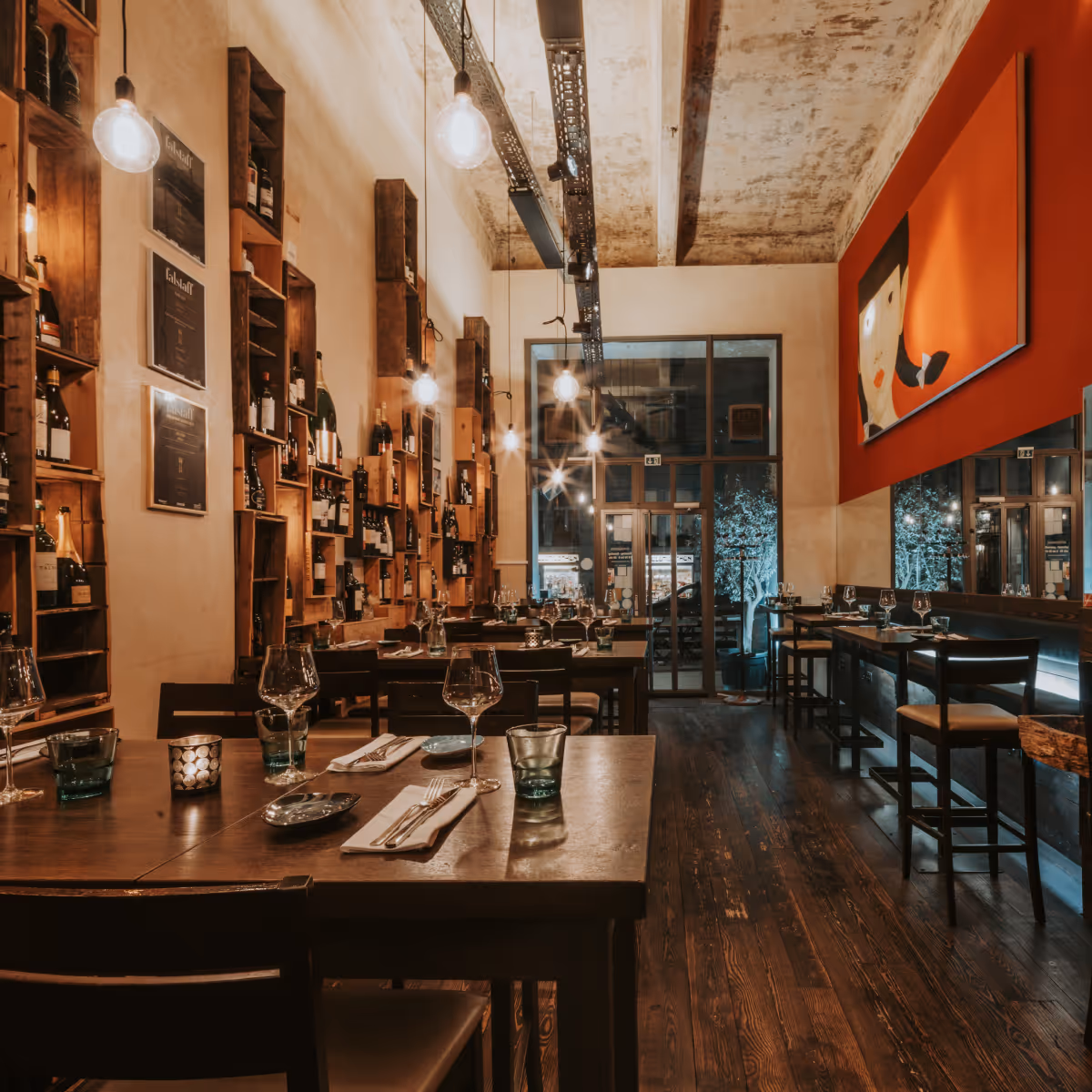 Gemütliches Restaurant mit Holzregalen voller Weinflaschen, gedeckten Tischen und modernem Deckenlicht.