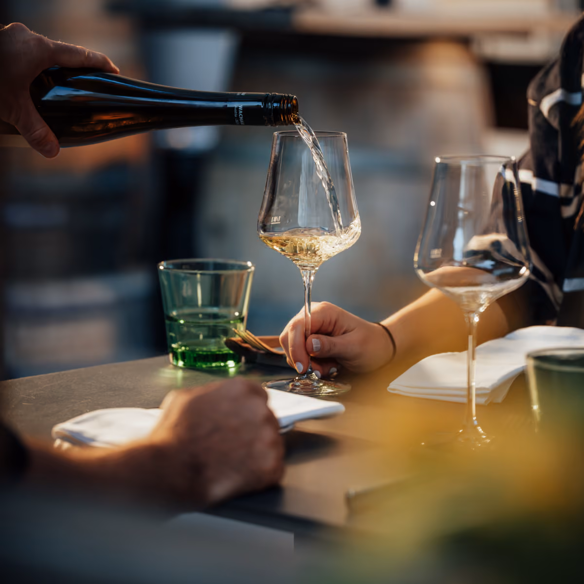 Jemand gießt Weißwein in ein Weinglas, während eine andere Person das Glas hält.