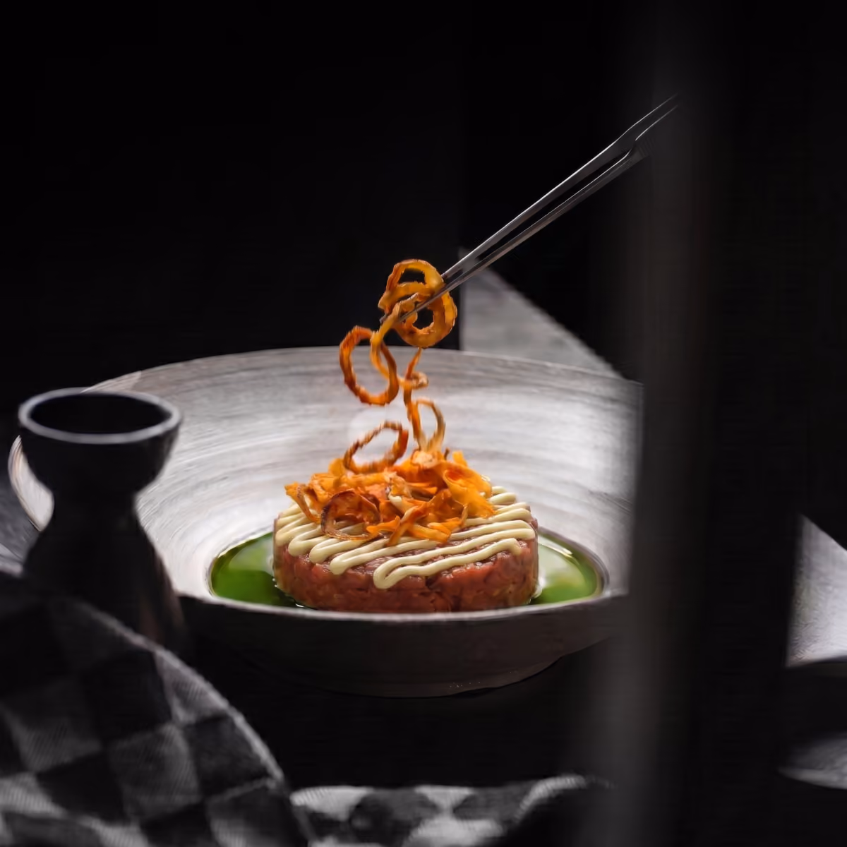 Feine Tatar-Runde mit Mayonnaise, darauf werden frittierte Zwiebelringe mit Pinzette platziert.