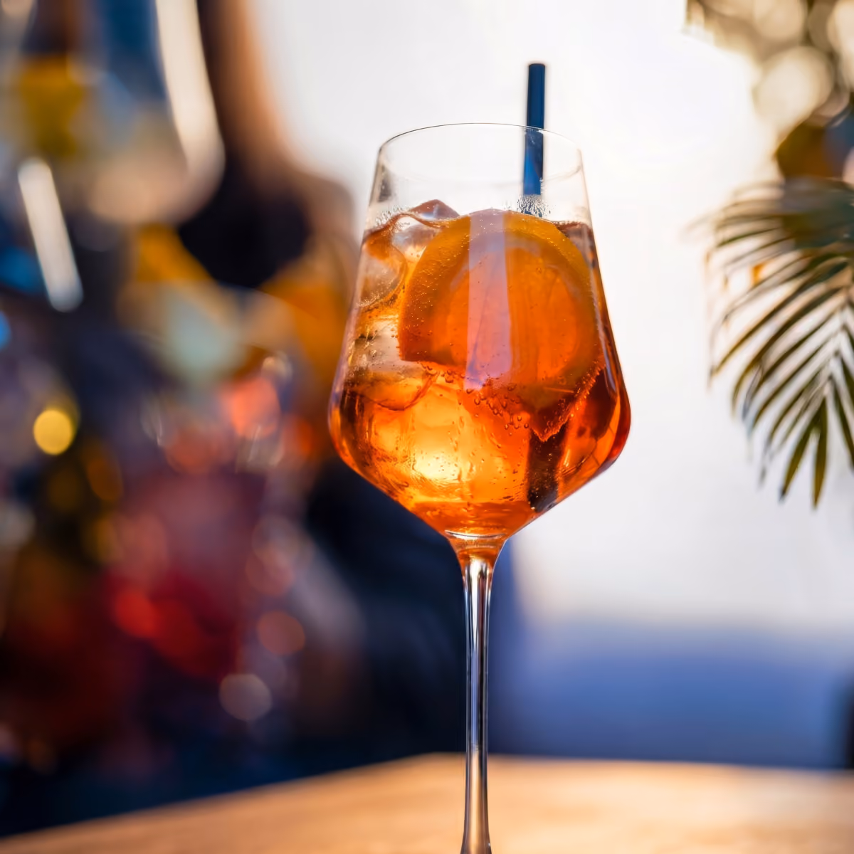 A glass with orange cocktail, ice cubes, an orange slice and a black straw.