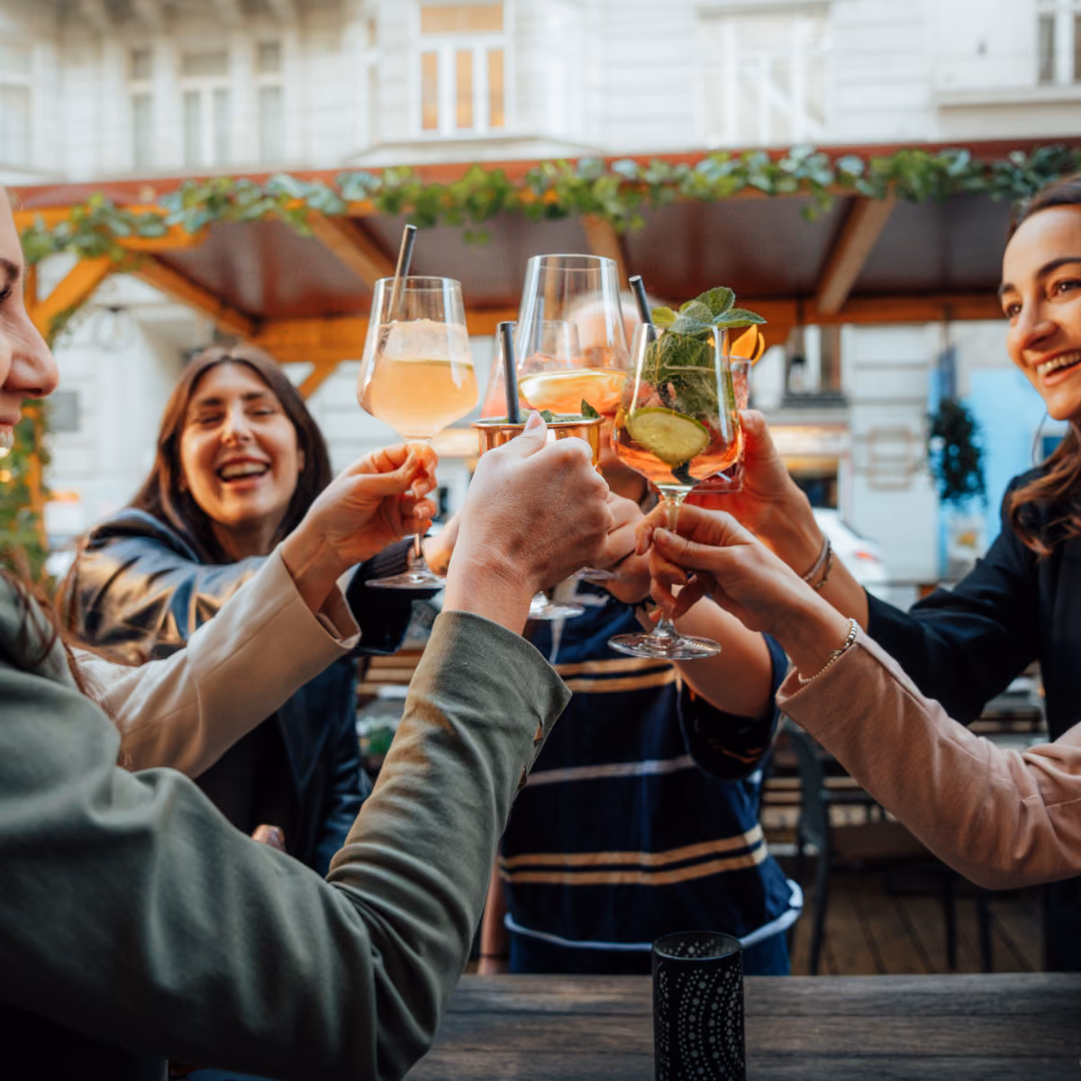 Freunde stoßen mit verschiedenen Cocktails an einem Outdoor-Tisch in entspannter Atmosphäre an.