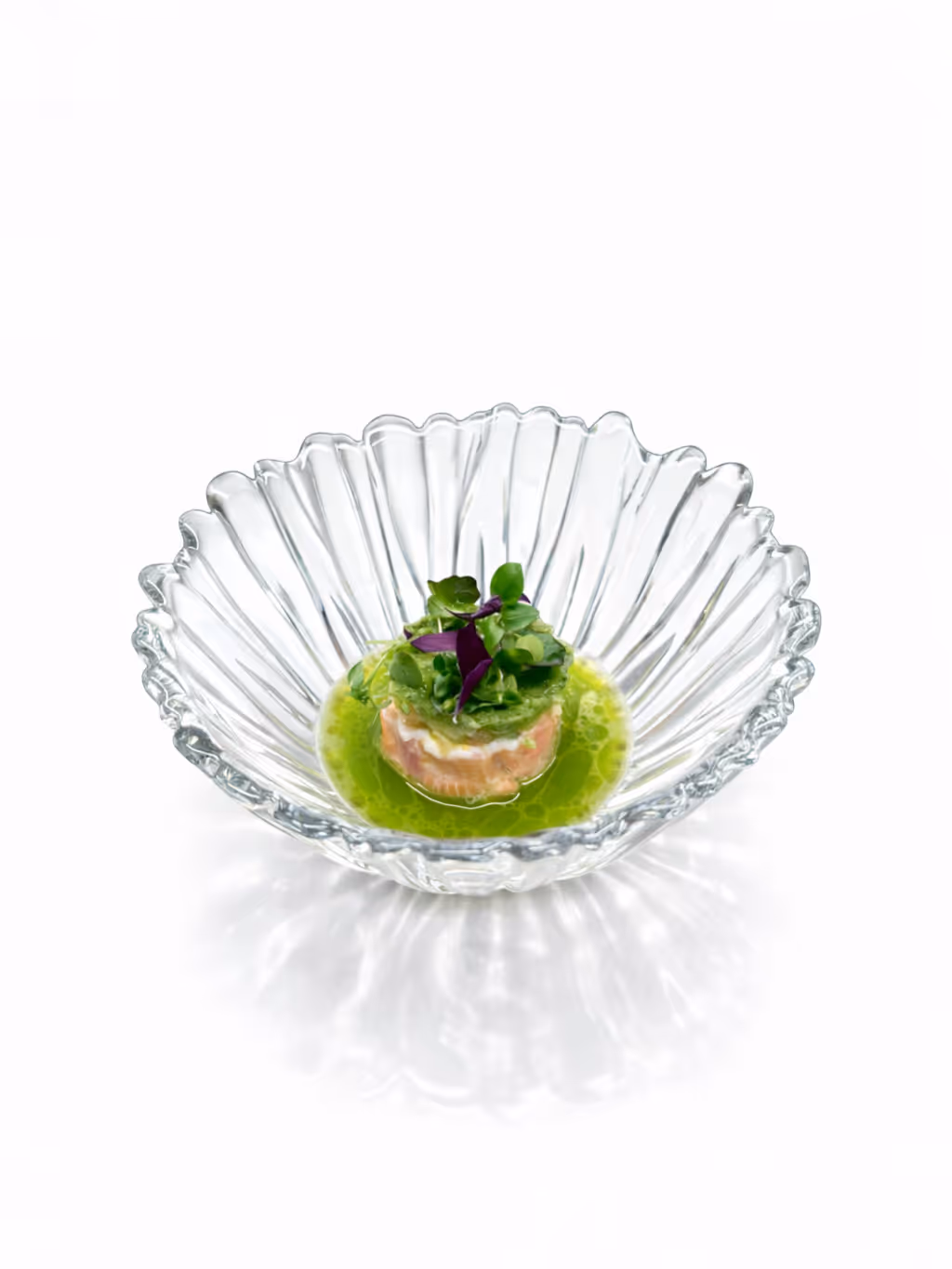 Feine Speise mit grünem Kräutersud in einer klaren, geriffelten Glasschale angerichtet.
