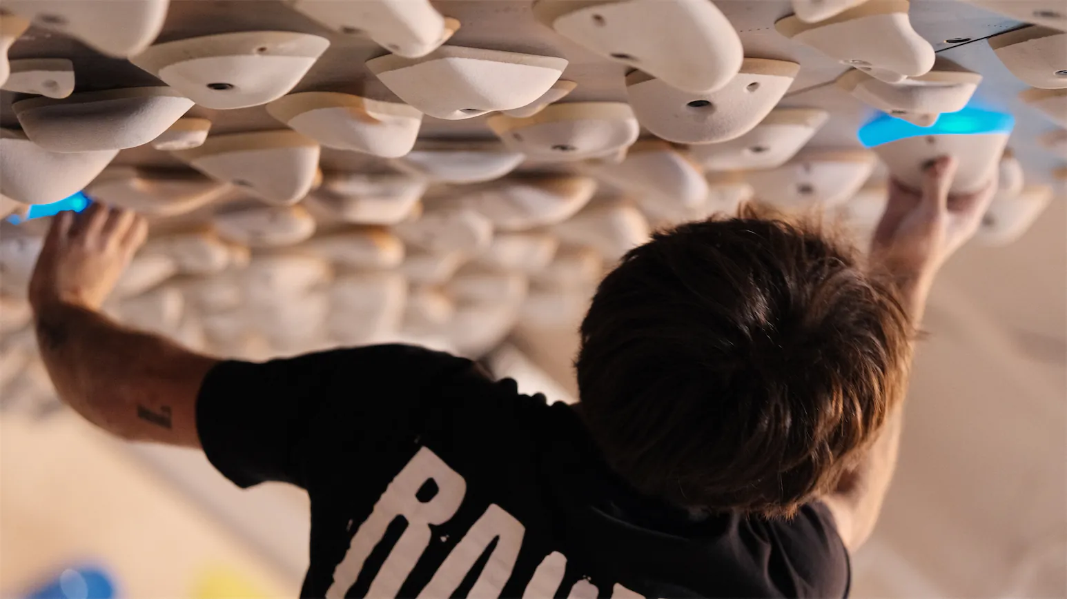 Grimpeur vu de près sur une board à prises lumineuses.