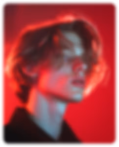 Blurred portrait of a person with medium-length hair against a red background.
