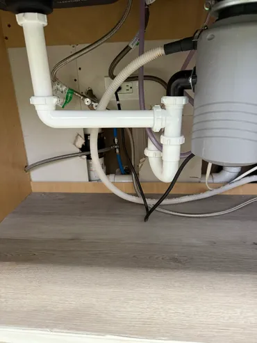 Under-sink plumbing setup with white PVC pipes and a garbage disposal unit attached.