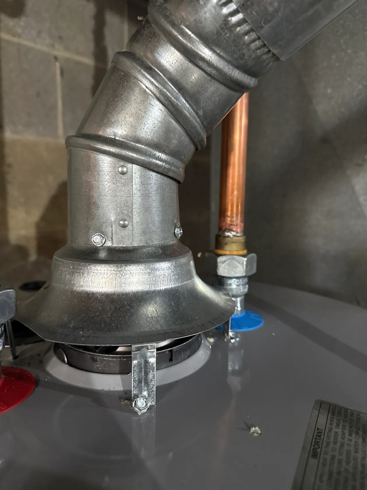 Close-up of metal vent pipe and copper water pipe connected on top of a water heater.