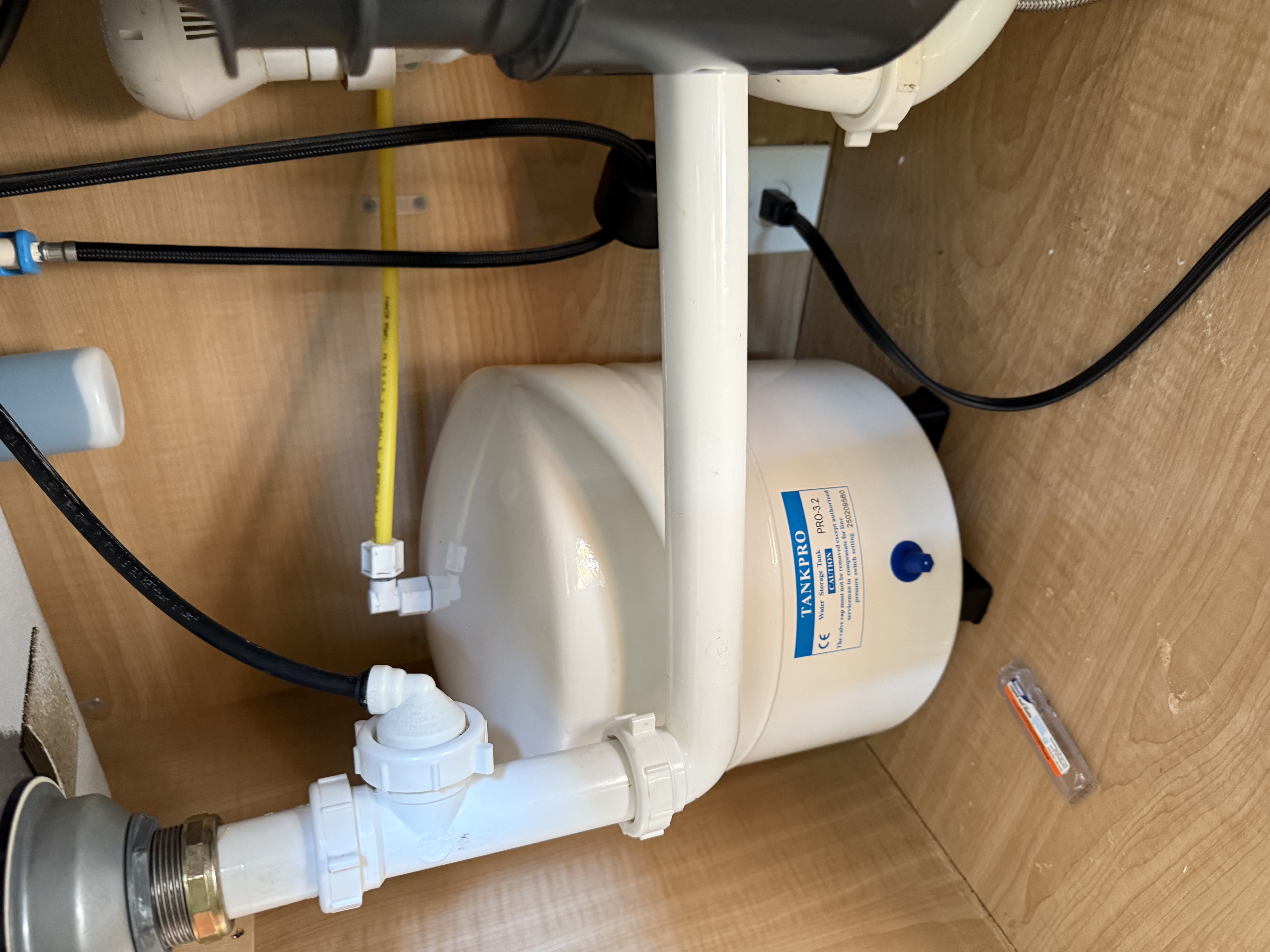 White TankPro water storage tank installed under a kitchen sink with connected pipes and hoses.