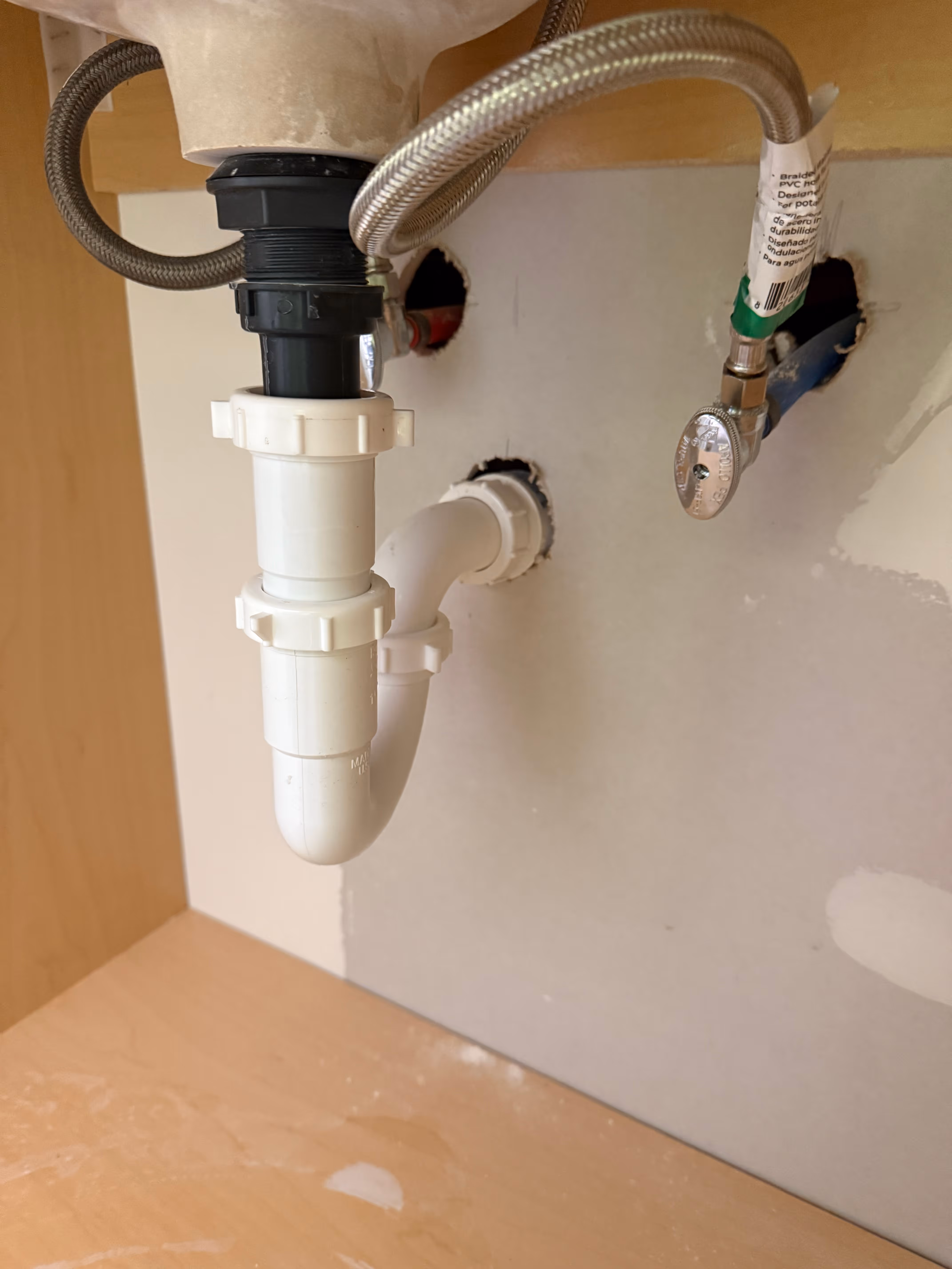 Under-sink kitchen plumbing showing white PVC pipe trap and flexible water supply lines connected to wall valves.