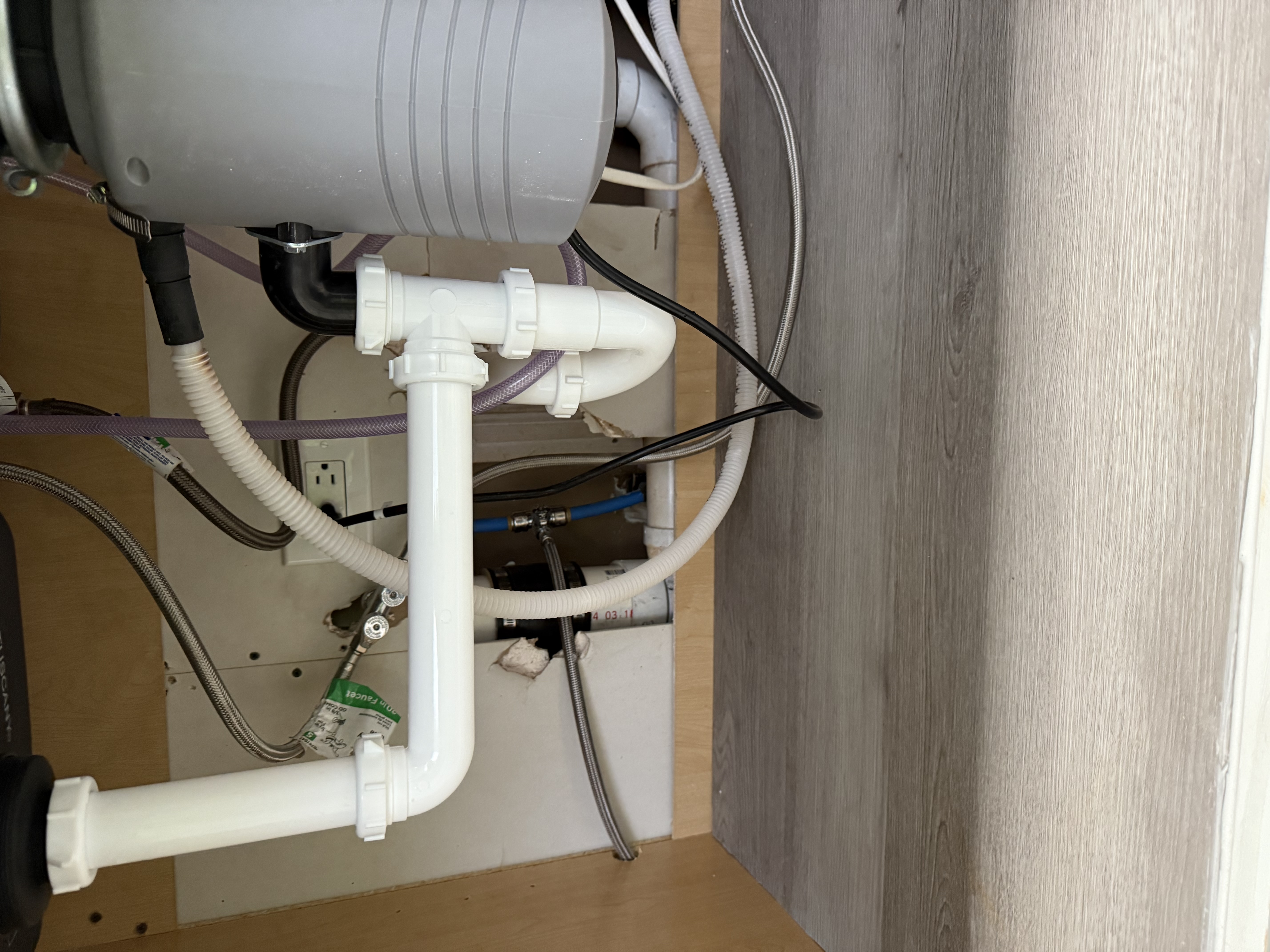 Under-sink plumbing piping and garbage disposal unit inside a wooden cabinet.