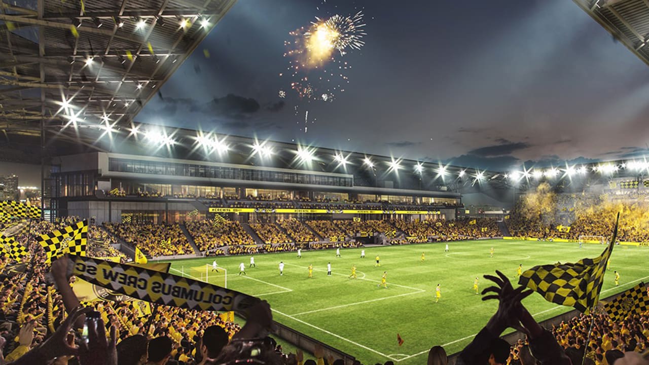 Nighttime soccer match in a stadium filled with fans waving yellow and black checkered flags, with fireworks in the sky.