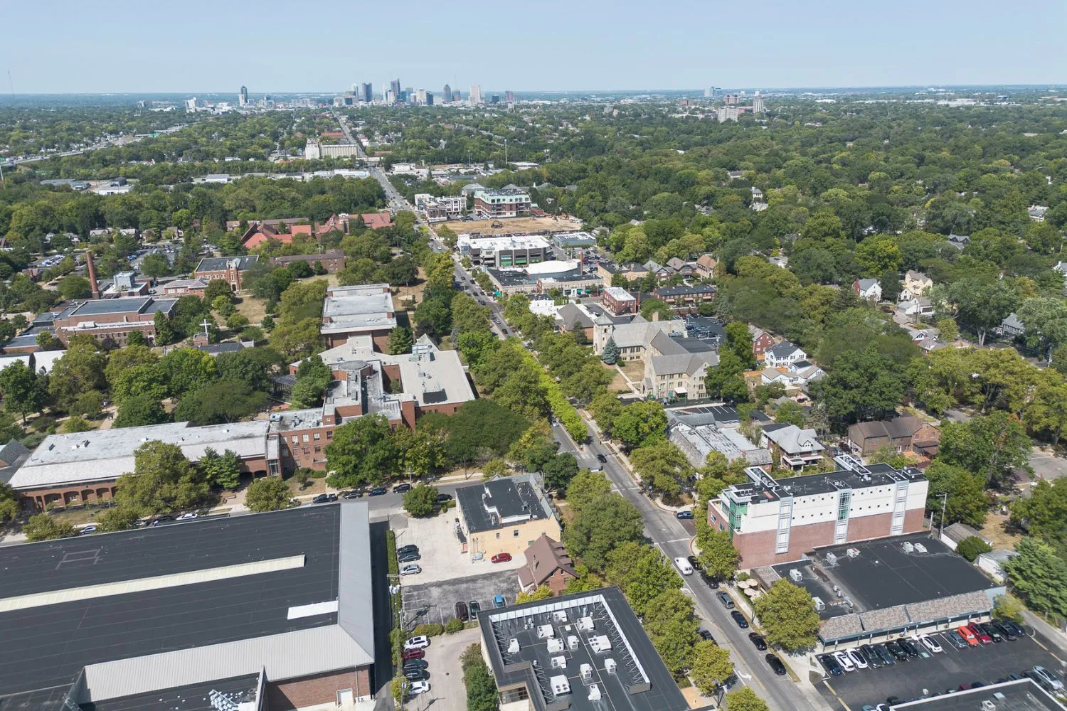 Aerial view of a suburban neighborhood with tree-lined streets, mixed residential and commercial buildings, and a distant city skyline in Bexley, Ohio.