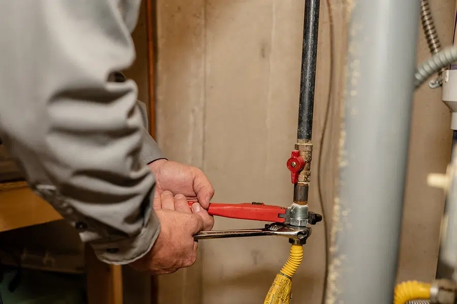 Person using a red pipe wrench and a silver wrench to tighten a gas line connection with a yellow flexible gas pipe and a red valve in Hilliard, Ohio.