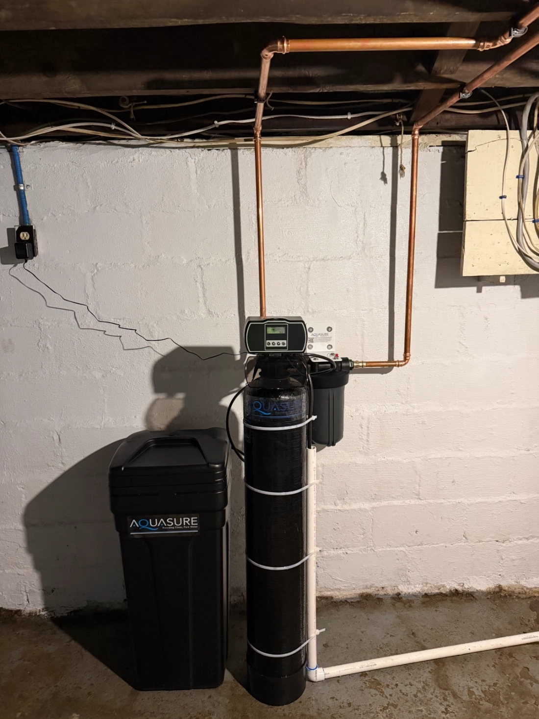 Aquasure water softener system installed against a basement wall with copper piping and a control display on top in Dublin, Ohio.