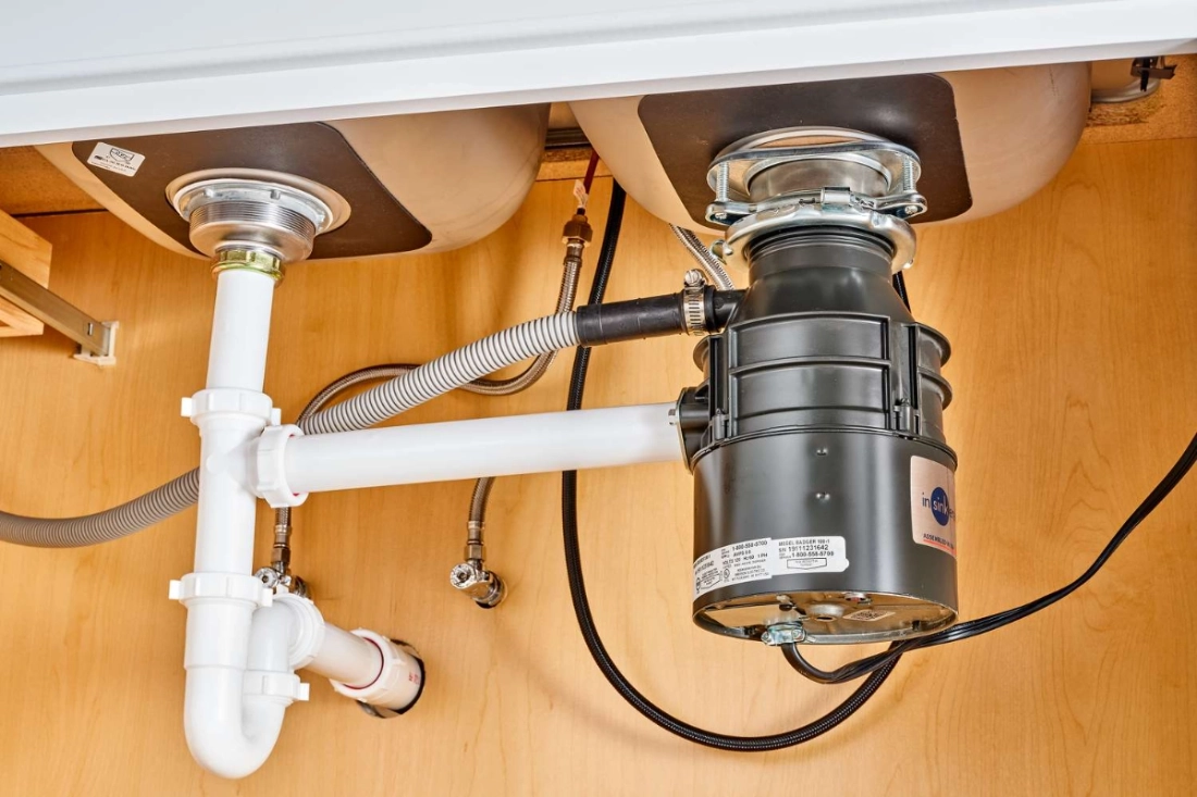 Garbage disposal unit installed under a kitchen double sink with connected plumbing pipes in Dublin, Ohio.