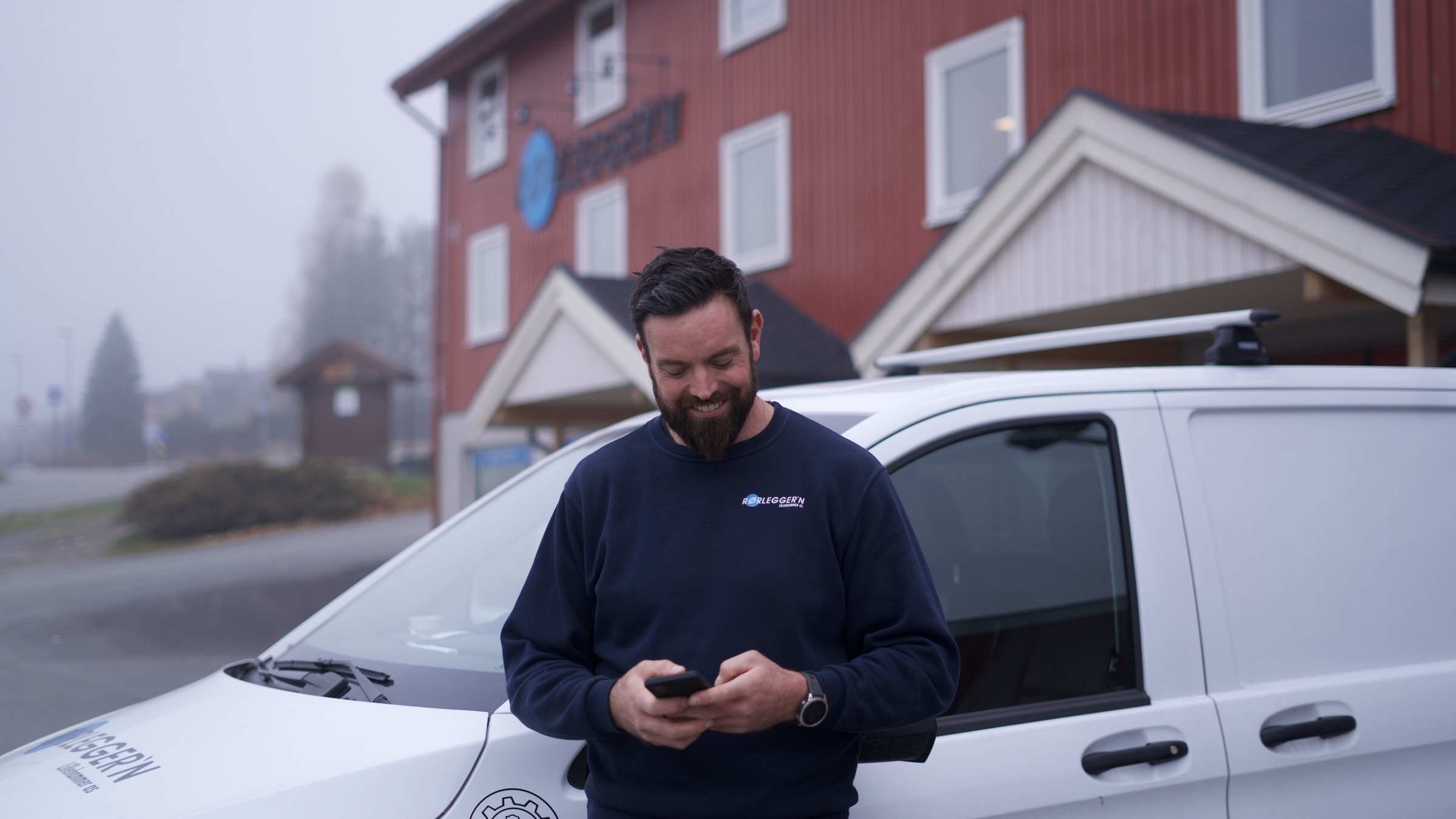 Rørlegger hos Rørlegger'n Lillehammer med telefonen i hånda foran servicebilen