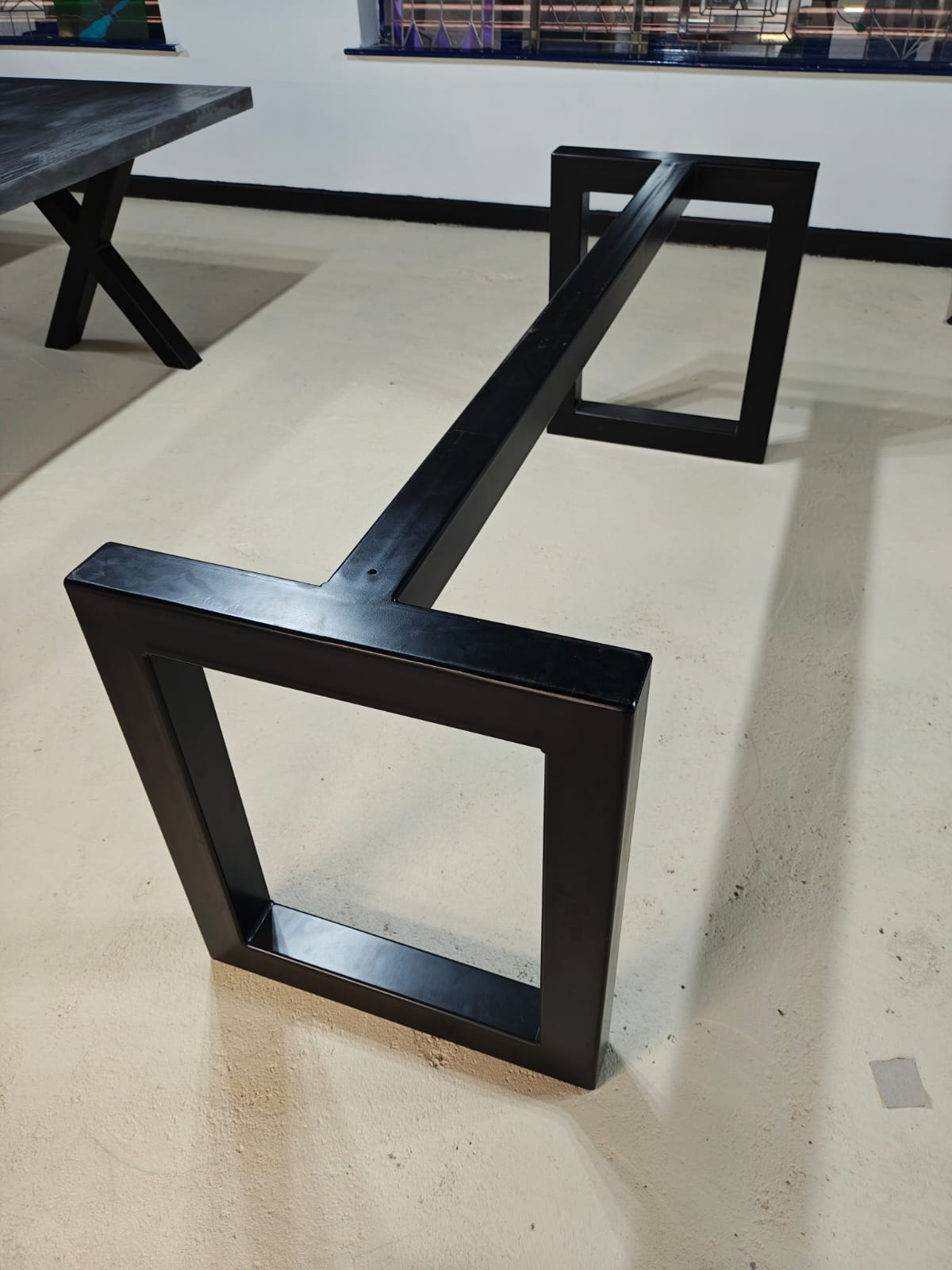 Black metal table base with two square legs connected by a horizontal bar on a light floor.