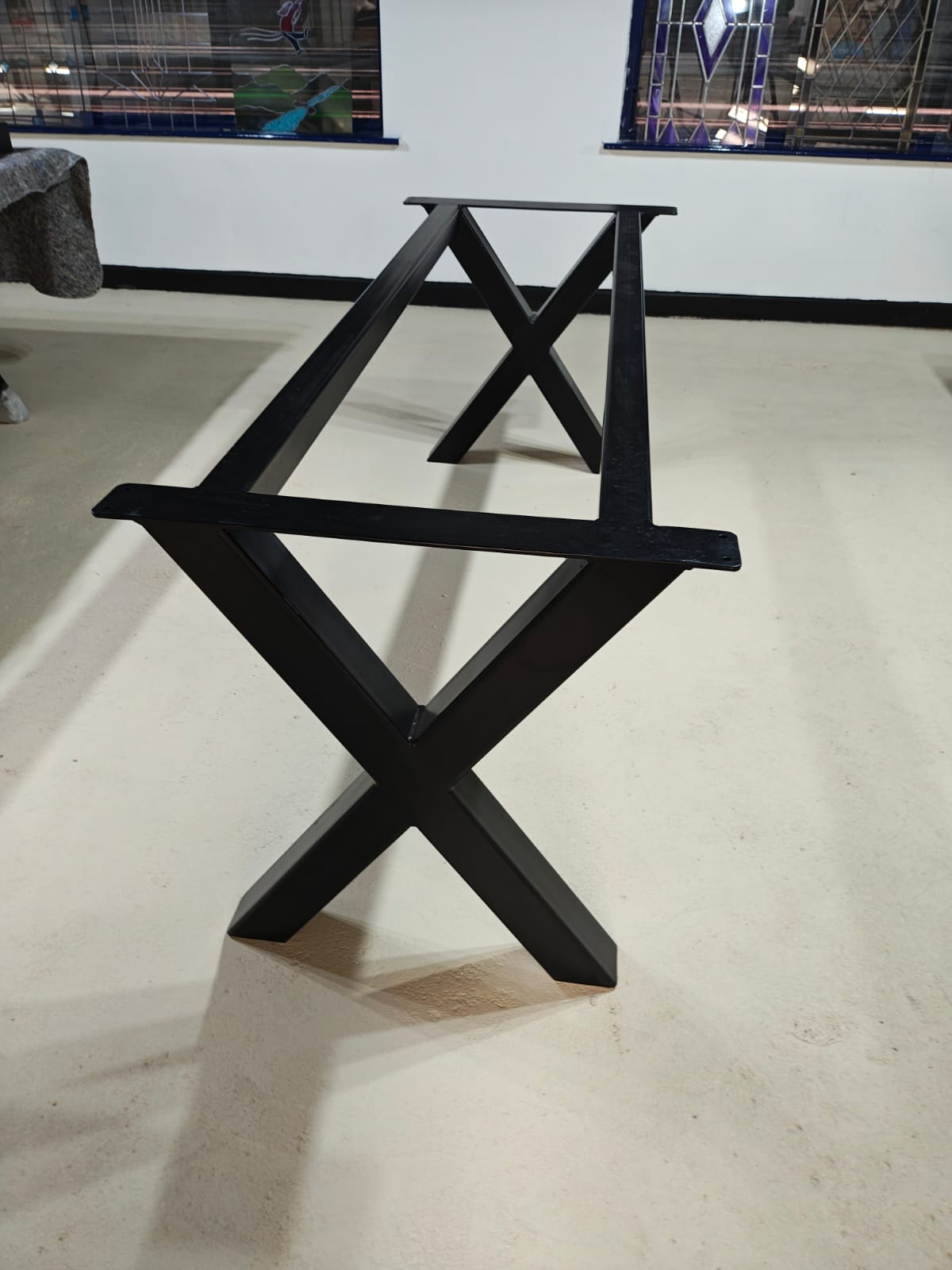 Black metal table base with X-shaped legs on a light-colored floor indoors.