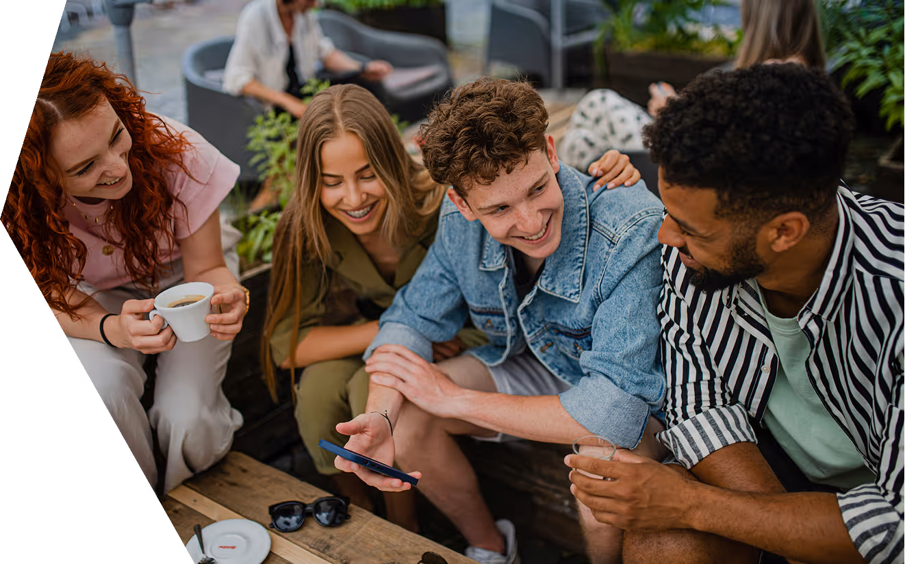 Group of four young adults sitting together, smiling, and looking at a smartphone.