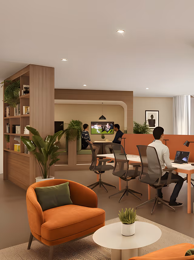 Modern office lounge with orange armchairs, a coffee table with a plant, and a workspace with people using laptops and sitting in a booth area.