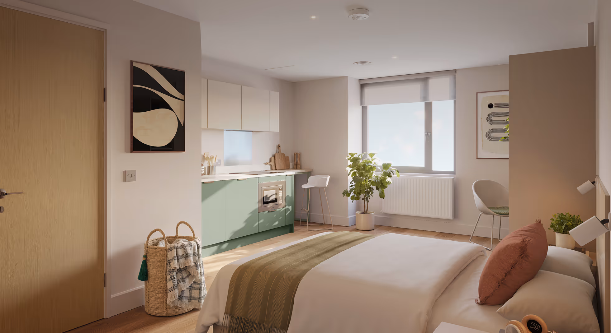Modern studio apartment with green lower kitchen cabinets, a bed with white and olive bedding, a window with a white roller blind, and a small potted plant near a chair.