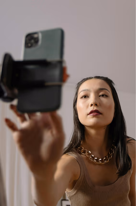 Woman with dark hair and a chunky gold chain necklace adjusting a smartphone on a tripod or holder.