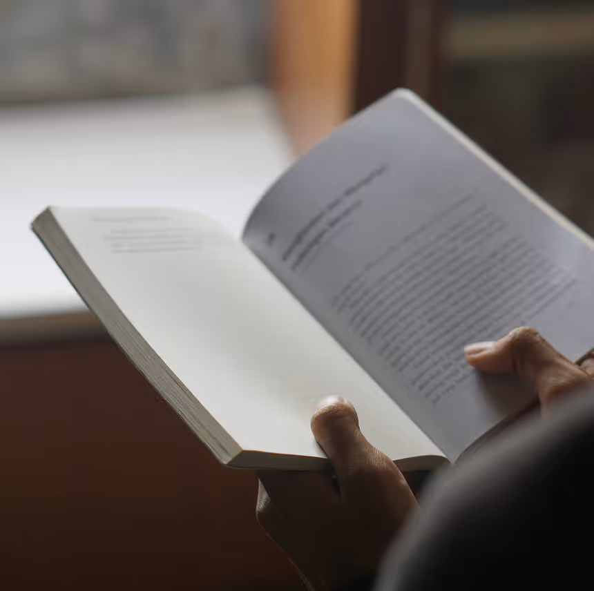 Close-up of hands holding and reading an open book with text on both pages.