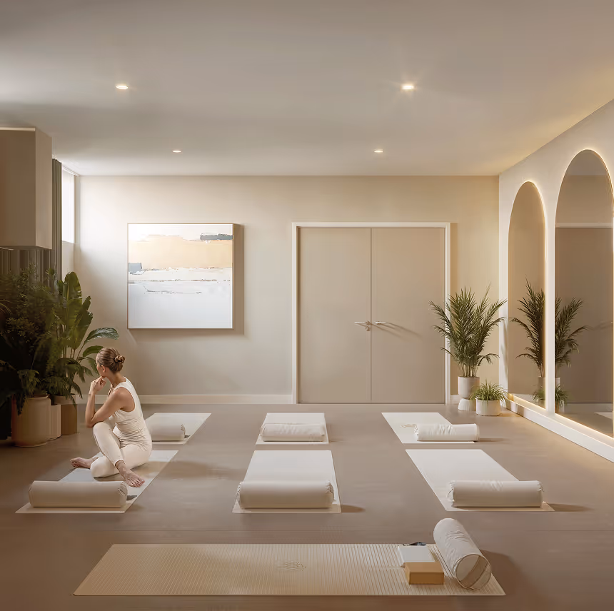Minimalist yoga studio with six white yoga mats arranged on the floor with bolsters, a woman sitting on one mat with legs crossed, large plants, arched mirrors, and soft ambient lighting.