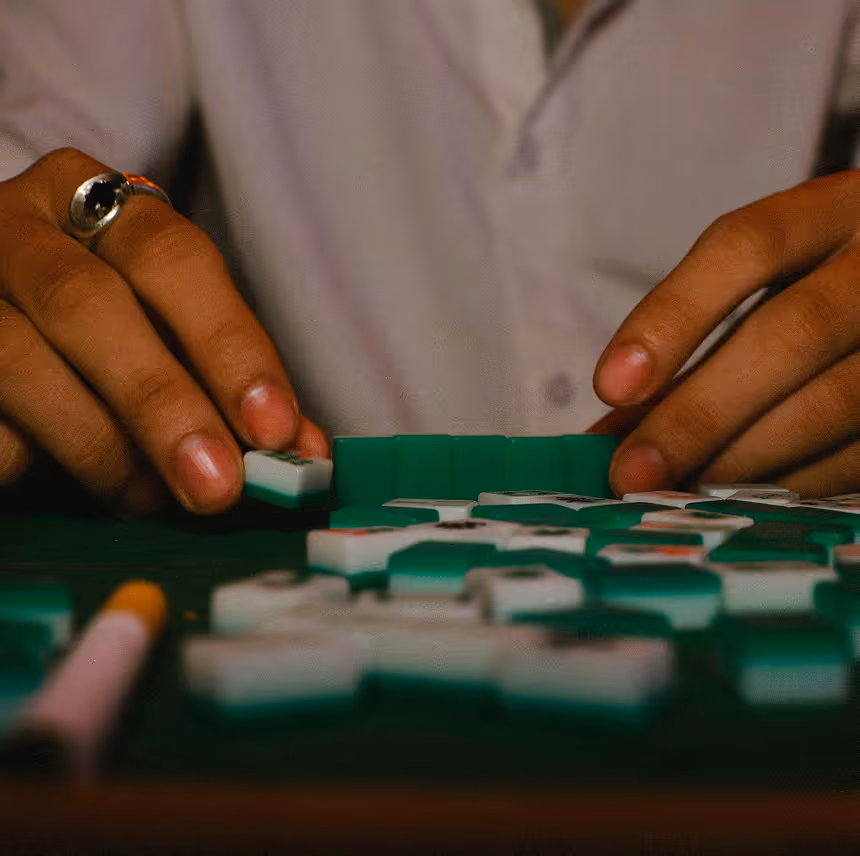 Hands with a ring organizing green-backed Mahjong tiles on a game table.