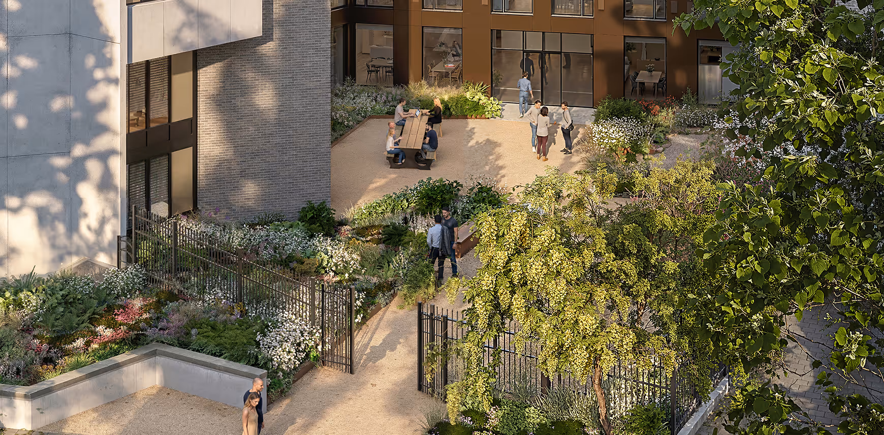 Sunlit private courtyard with trees, flower beds, gravel paths, seating areas, and people socializing near a building entrance.