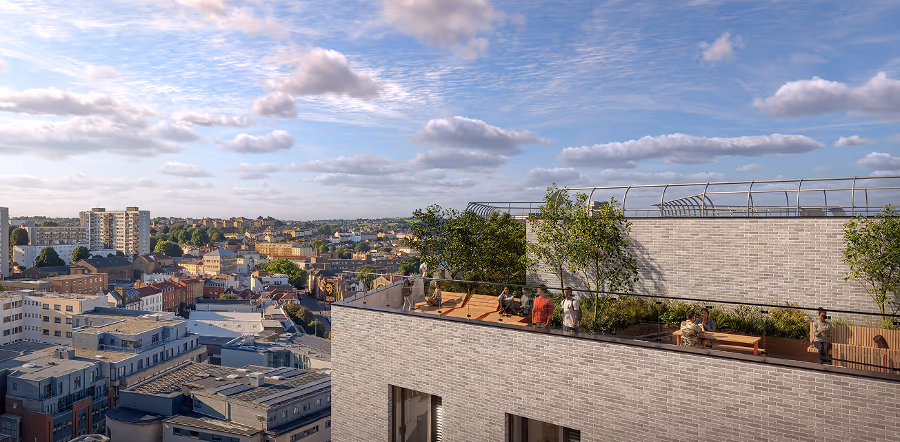 Rooftop terrace with wooden benches, glass railing, trees, and people relaxing overlooking a cityscape under a partly cloudy sky.
