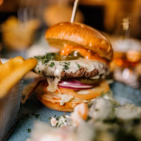 Cheeseburger with melted cheese, lettuce, tomato, red onion, and pickles on a brioche bun, served with fries and a side salad.
