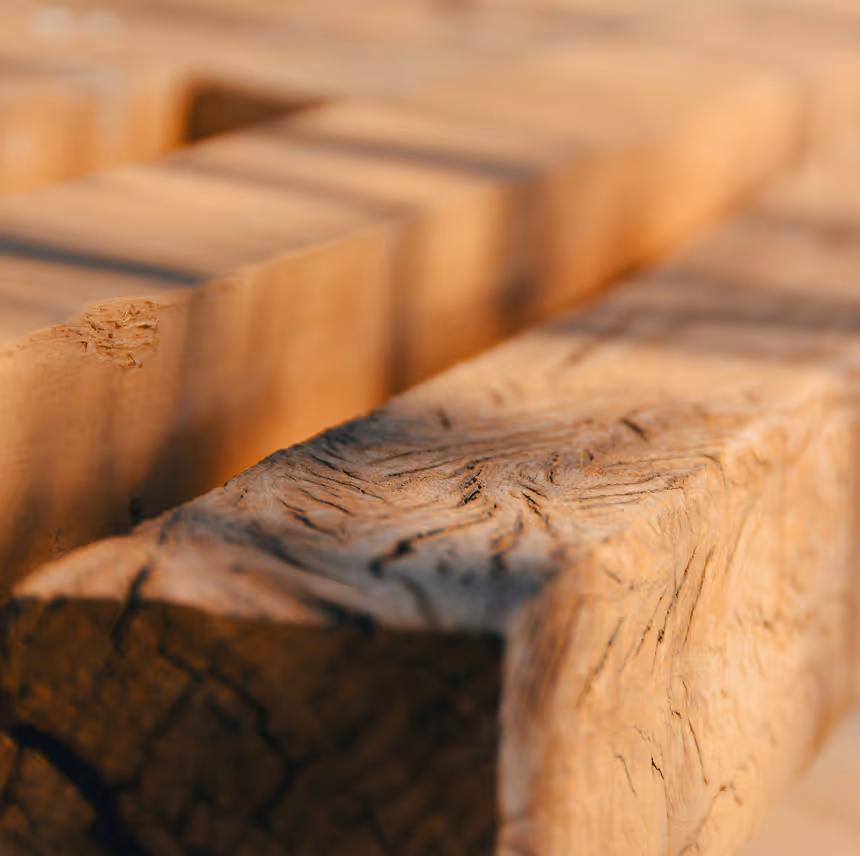 Close-up of textured wooden beams with natural grain and cracks, softly lit by warm light.