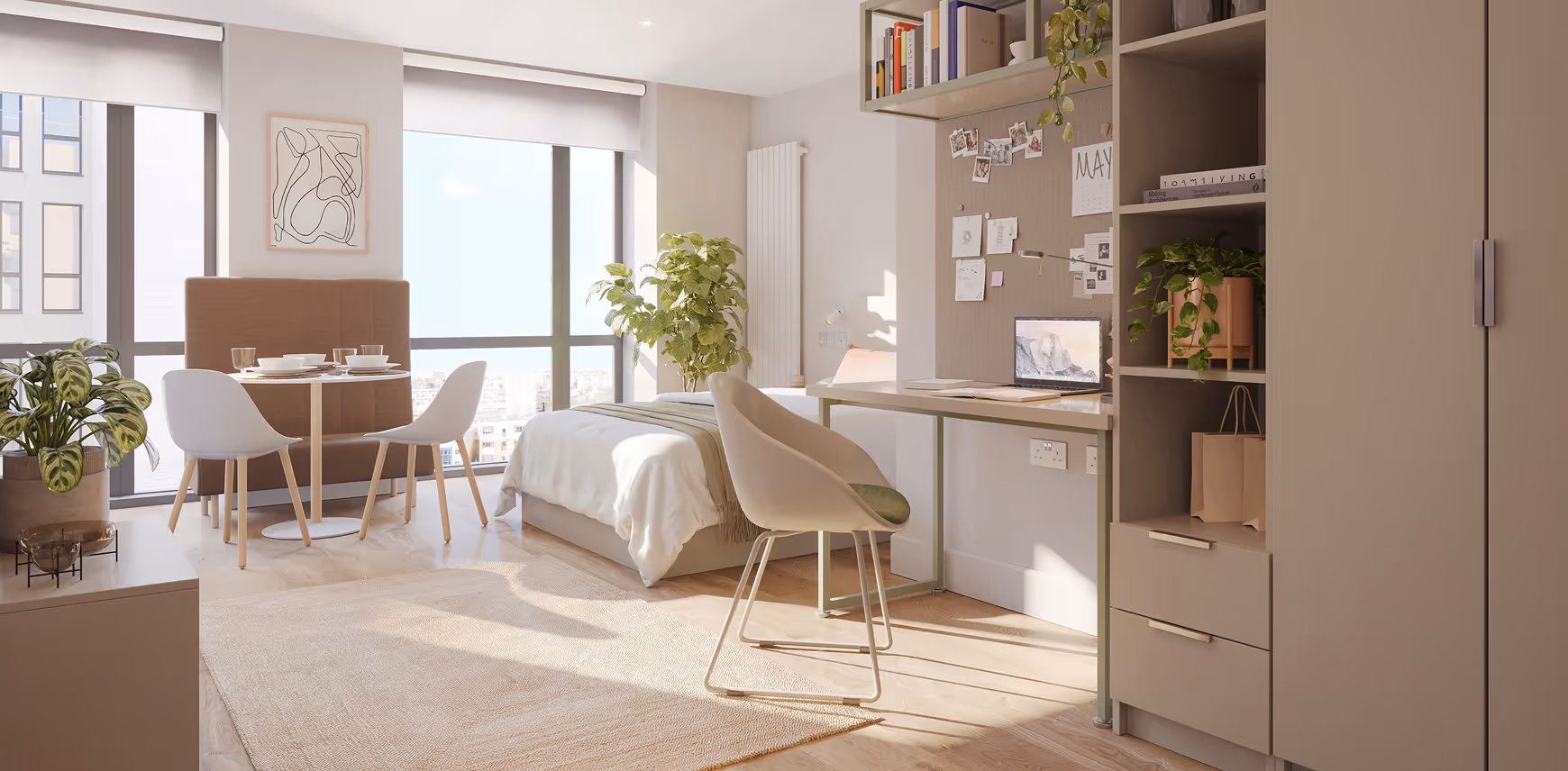 Bright modern studio apartment with a bed, dining table with chairs, desk with laptop, and plants near large windows.