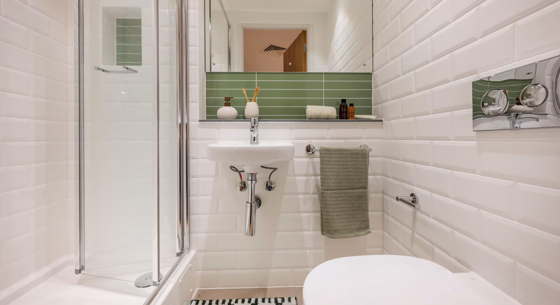 Small modern bathroom with white subway tiles, a glass shower, wall-mounted sink, green towel, and green tiled backsplash under mirror.