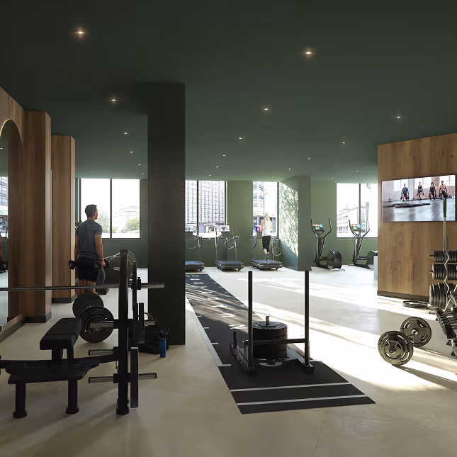 Modern gym interior with weightlifting bench, sled push equipment, treadmills, elliptical machines, and a man holding dumbbells near a large window.