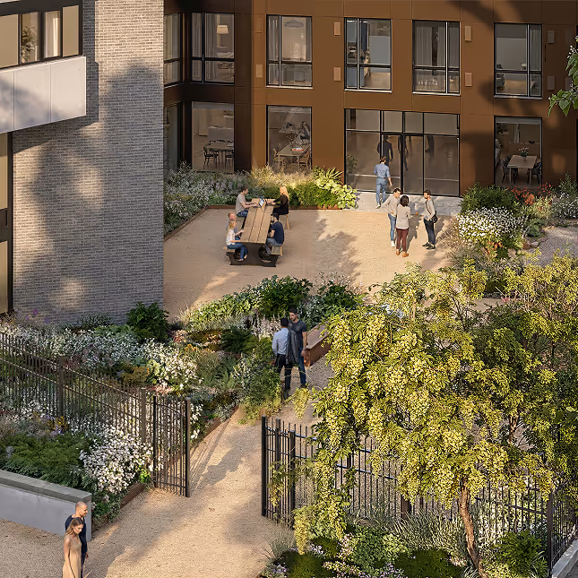 A sunny courtyard with people sitting at a picnic table, others standing and talking, surrounded by lush greenery and flowers near apartment windows.