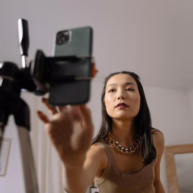 Woman with long dark hair adjusting smartphone on tripod for filming or video call.