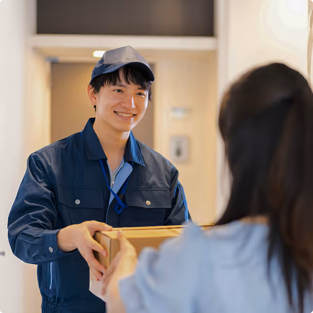 Smiling delivery man in blue uniform handing a package to a woman indoors.