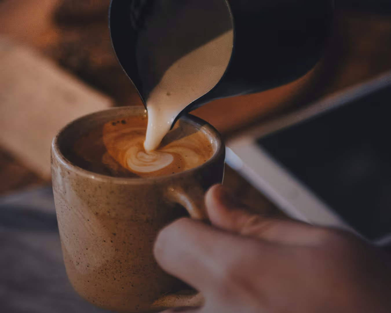 Close-up of milk being poured from a black jug into a brown ceramic cup of coffee.