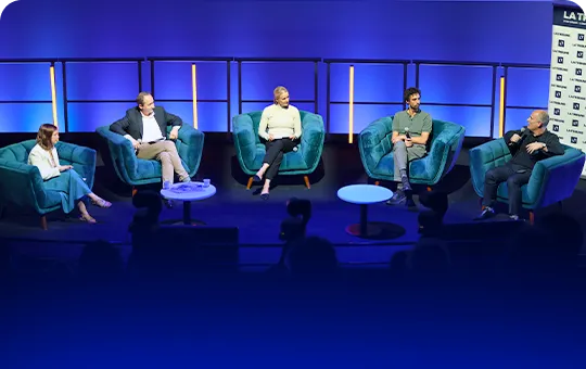 Cinq intervenants assis sur des fauteuils bleus sur scène lors d'un panel de discussion.