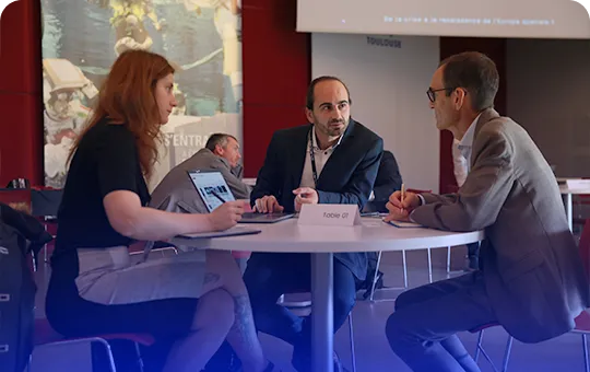 Trois personnes discutent sérieusement autour d'une table ronde lors d'un forum professionnel.