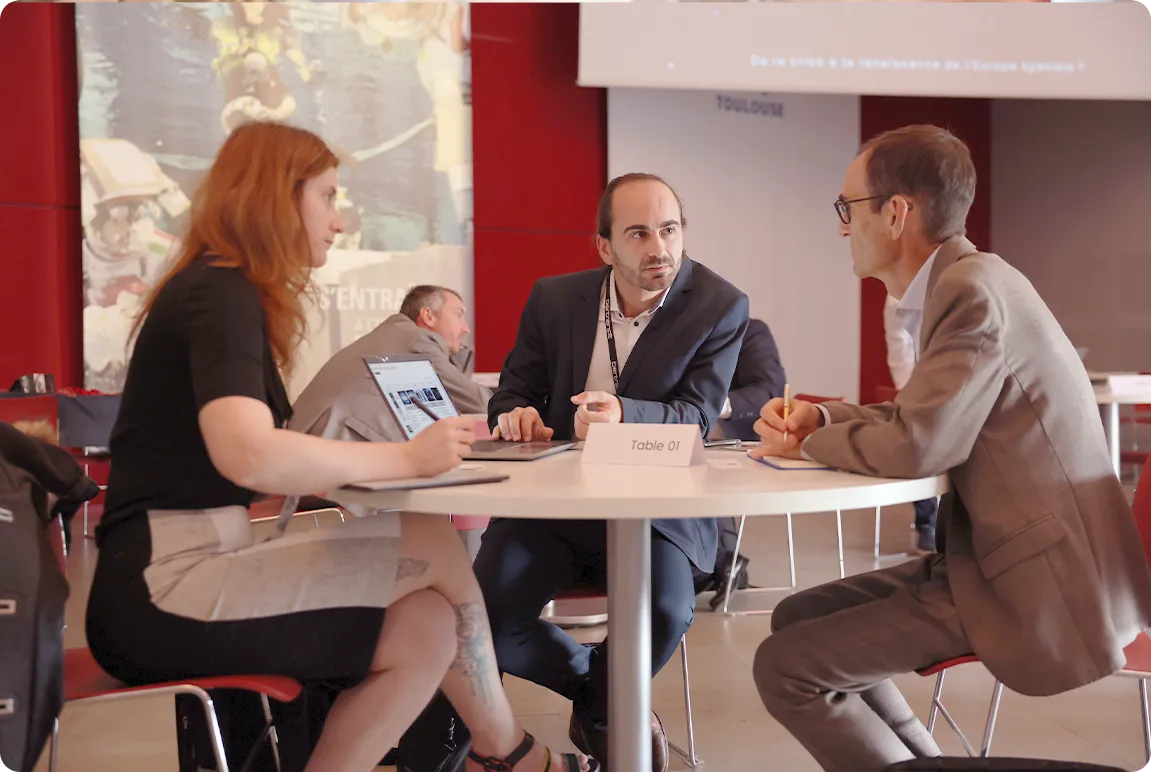 Trois personnes en réunion d'affaires assises autour d'une table ronde avec un ordinateur portable.