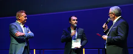 Trois hommes en costume discutent sur scène pendant une conférence.